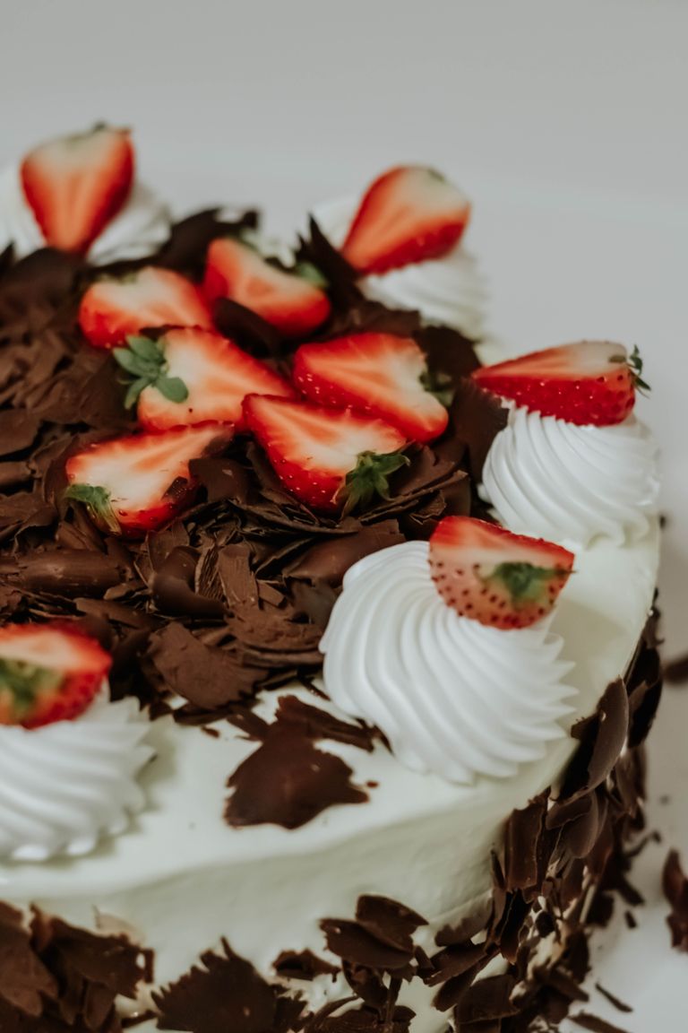 A tempting chocolate cake topped with strawberries and cream swirls, perfect for dessert lovers.