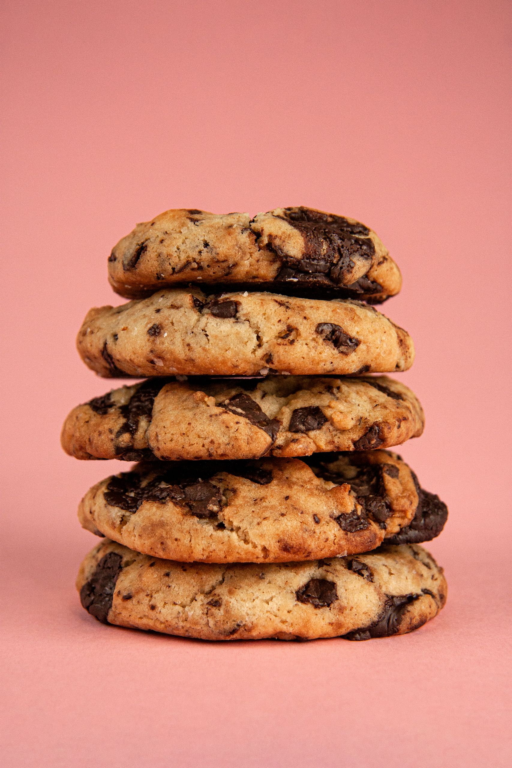 Delicious stack of freshly baked chocolate chip cookies on a vibrant pink backdrop.