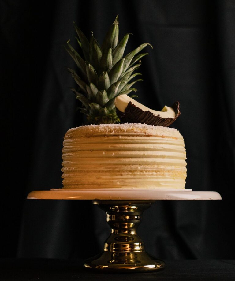 Elegant pineapple-topped cake on gold stand, perfect for celebrations.